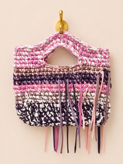 Multicoloured woven bag with fringe hanging on a hook against a beige background