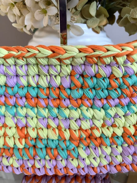 A close-up of a woven or braided textile product in vertical stripes of pastel orange, mint green, lavender, and turquoise, with a braided border on the left side. 