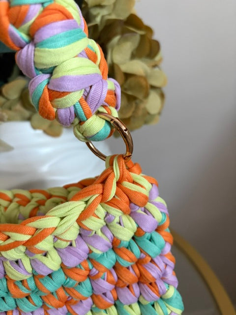 Close-up of a colorful braided fabric bag strap with a gold-tone metal ring, showing pastel orange, mint green, lavender, and pale yellow ribbed material.
