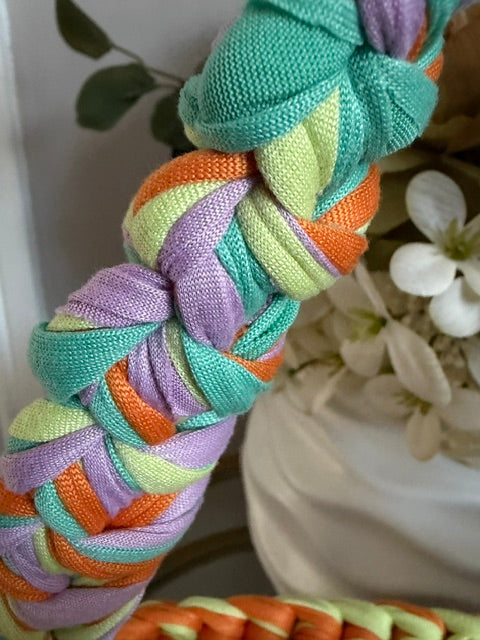 A close-up of a braided handle from woven fabric in pastel rainbow colours including mint green, orange, lavender, and pale yellow