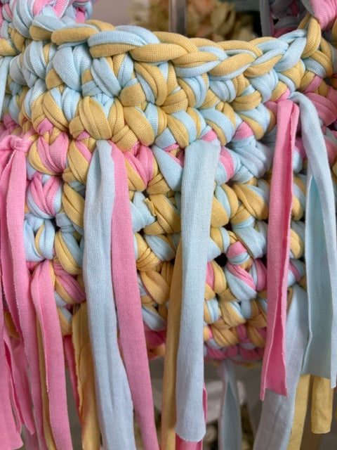 Close-up of a handmade braided bag made from pastel-colored fabric strips, featuring shades of pink, light blue, and yellow.