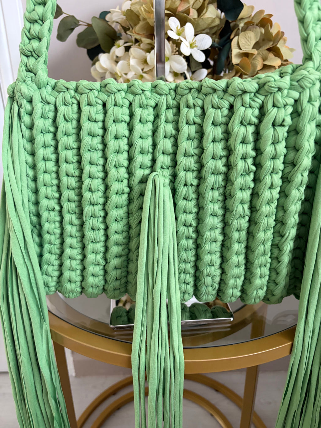 A close-up of a mint green chunky crochet handbag with matching woven strap