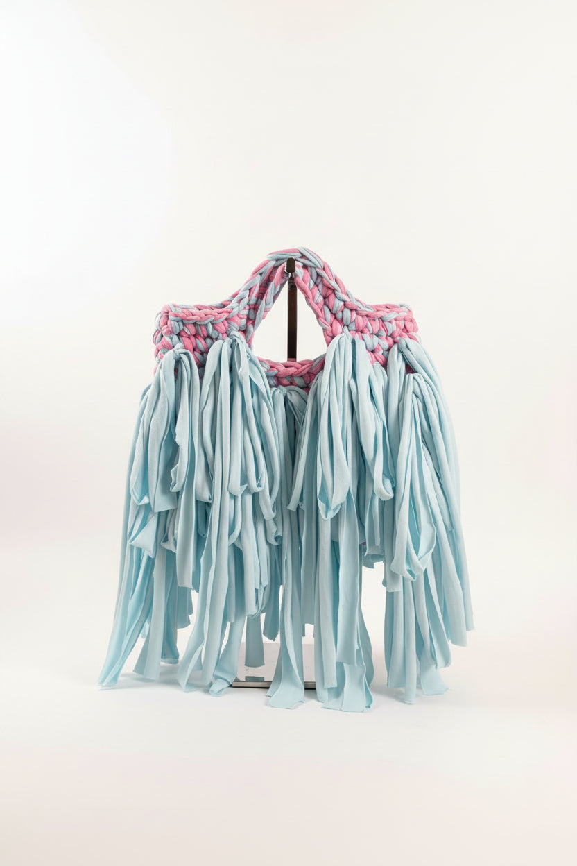 A handmade crochet bag made from pink and blue yarn with a light blue fabric fringe