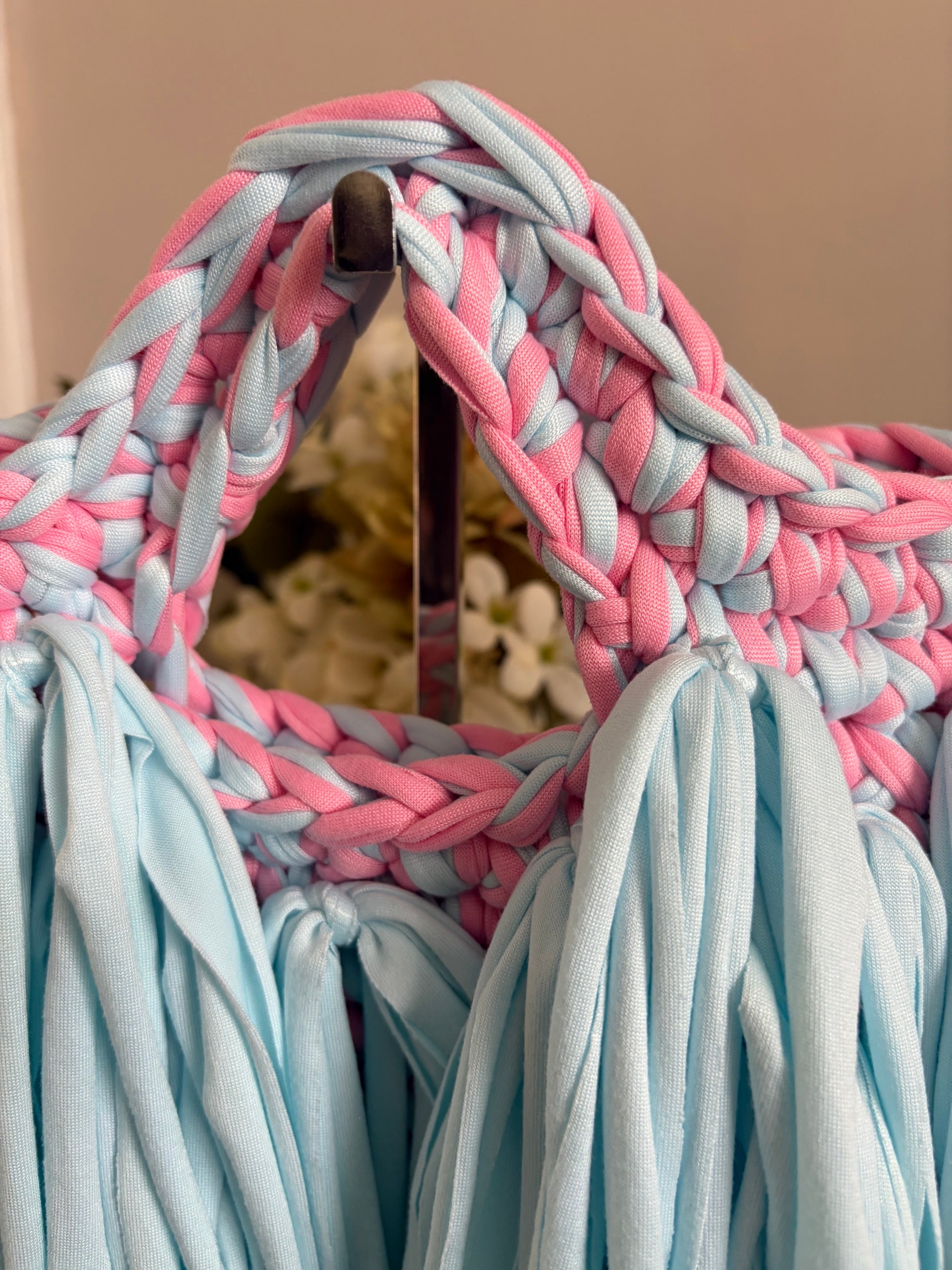 Close-up of a braided woven handle made from alternating light blue and pink fabric strips