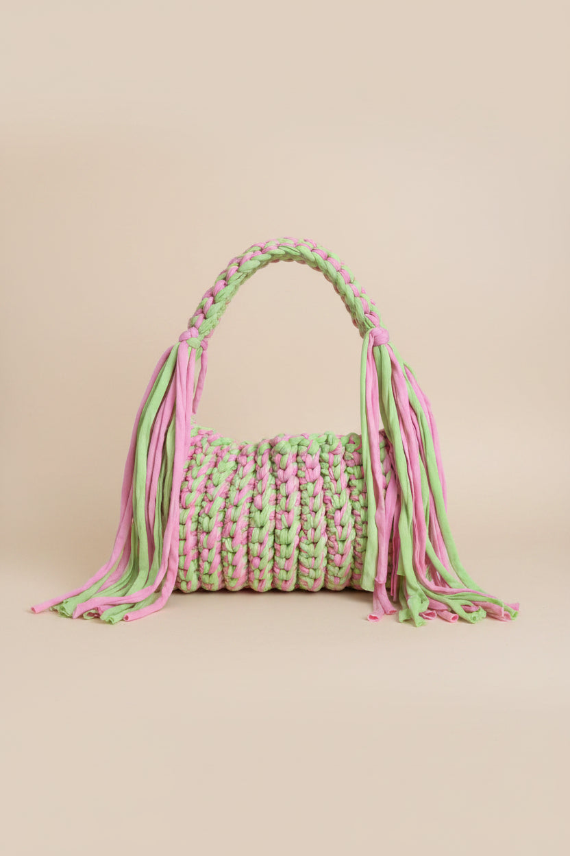 A close-up of a chunky braided crochet bag in alternating pastel pink and light green yarn