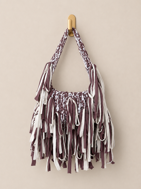 Handbag with fringe details hanging on a beige wall